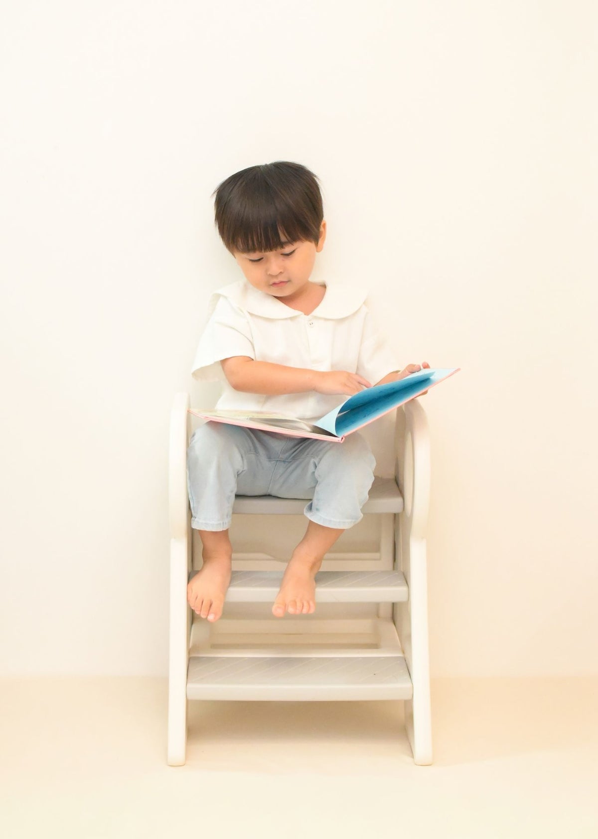 男の子が2段・3段可変式踏み台に座りながら本を読んでいる使用イメージ