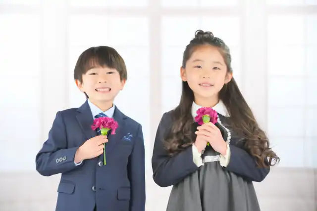 フォーマルな服を着た2人の笑顔の子供がピンクの花を持っています。