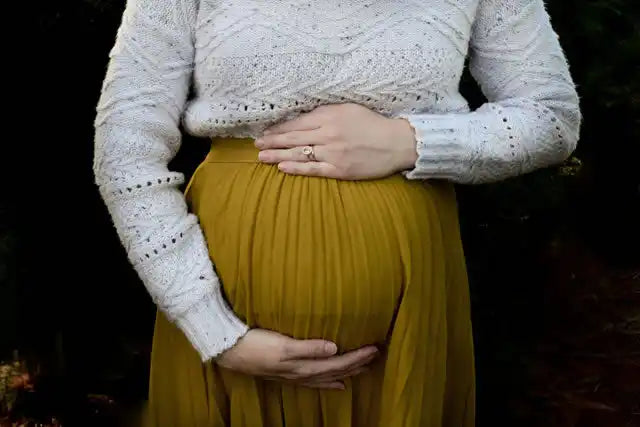 マスタードイエローのドレスを着た妊婦の腹が手によって支えられている。