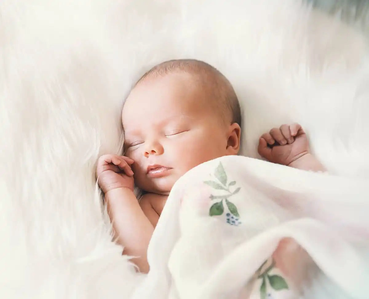 花柄のデザインの白い毛布に包まれた眠っている新生児の赤ちゃん。