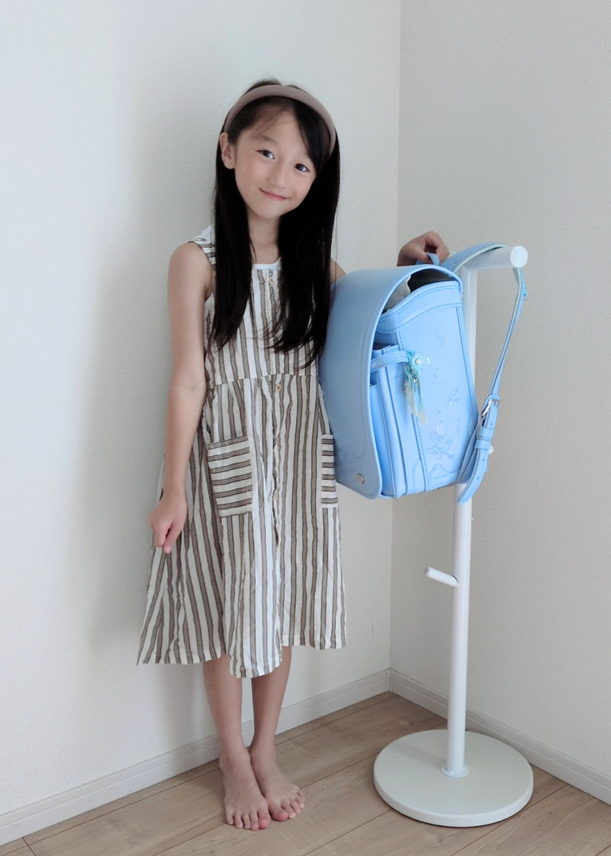 女の子がブルーのランドセルをランドセルスタンドに掛けている使用イメージ。通学用品を一か所にまとめて収納