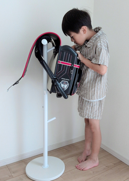 男の子がブラックのランドセルをランドセルスタンドに掛けている使用イメージ。帰宅後の片付けや翌日の準備に使える収納スタンド