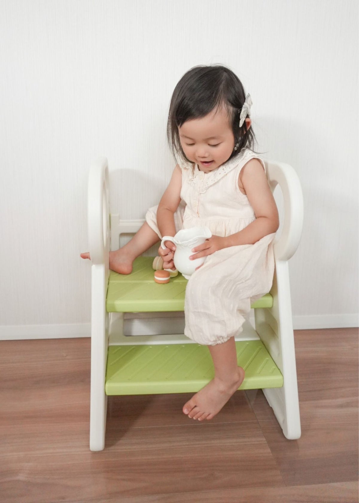 女の子がグリーンの2段・3段可変式踏み台に座っている使用イメージ。ワイドステップで足を置きやすい設計