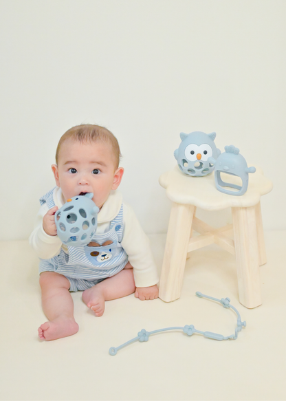 赤ちゃんがブルーのボールタイプのベビーシリコン歯がためを握っている使用イメージ。付属ストラップも写っている商品写真