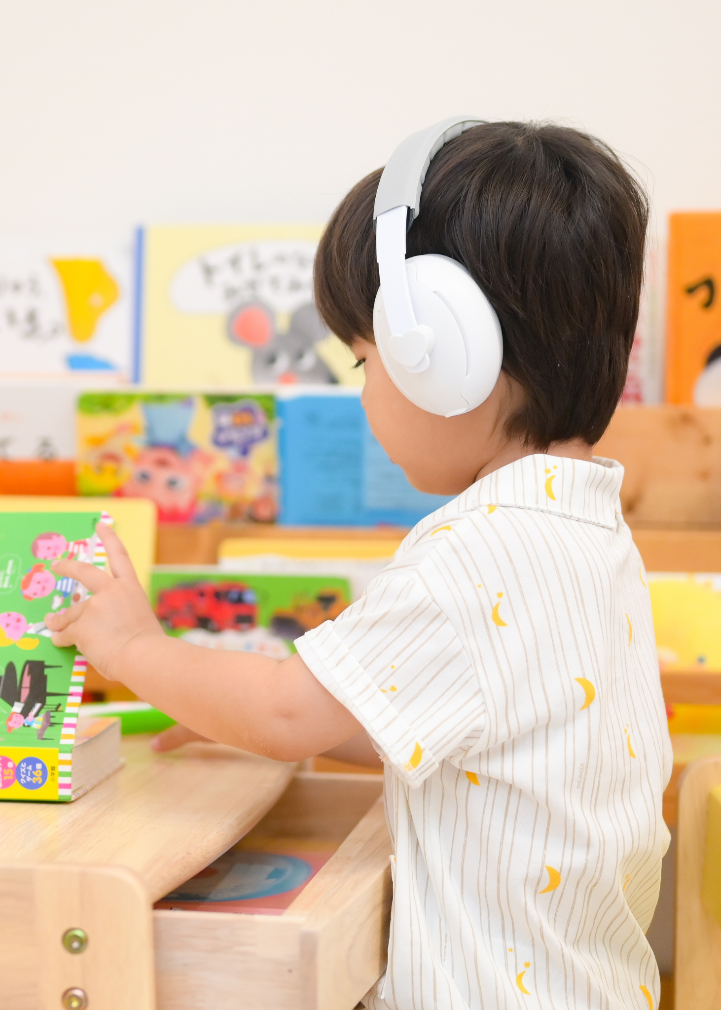 白い防音イヤーマフを子どもが着用している使用イメージ。室内で遊びながら装着している様子