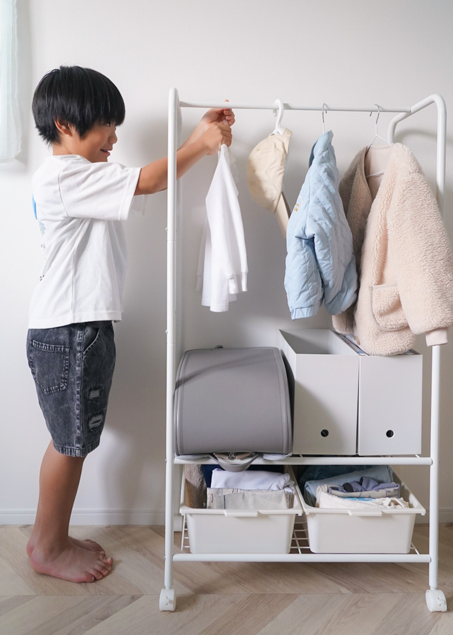 子どもがキッズハンガーラックに洋服を掛けている使用イメージ。自分で片付けやすい高さ設計