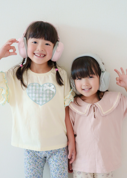 ピンクとホワイトのキッズ防音イヤーマフを姉妹が着用している使用イメージ。2人で並んで笑顔を見せる様子