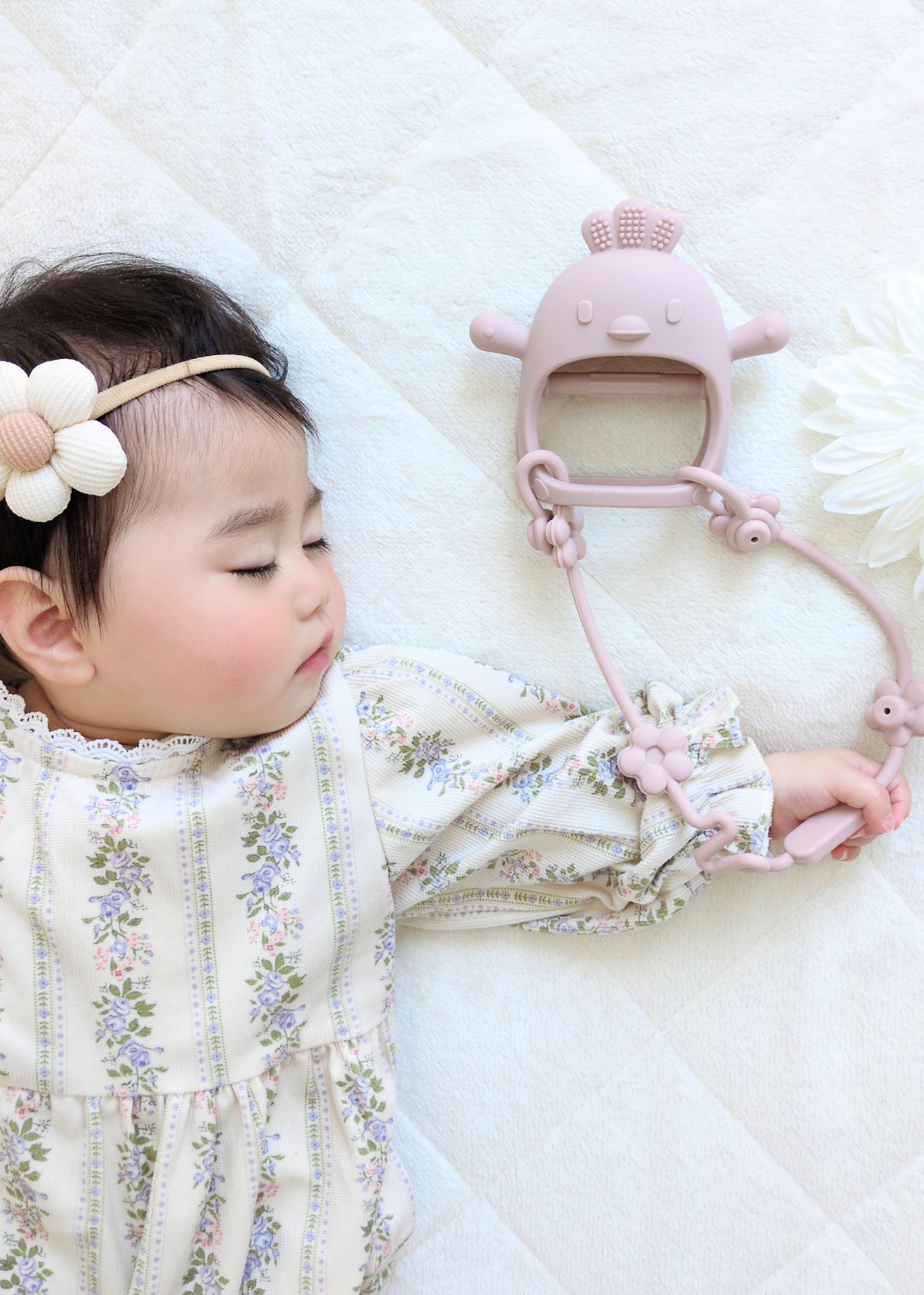 赤ちゃんがピンクのベビーシリコン歯がためを使っているイメージ。ベビーベッドでストラップ付き歯固めを手に取る様子