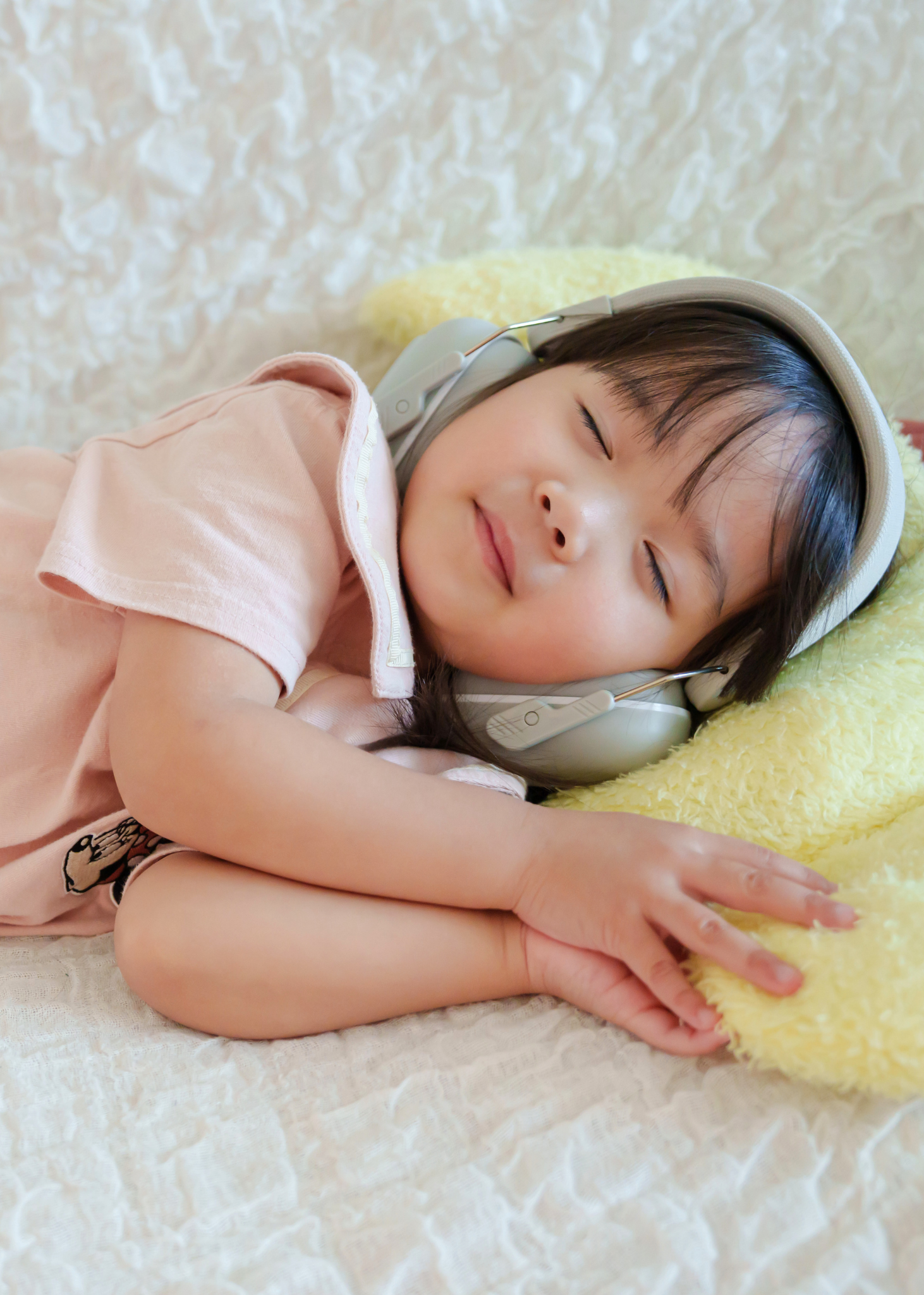 グレーの防音イヤーマフを女の子が着用して眠っている使用イメージ。休憩中や静かに過ごしたい場面での着用例