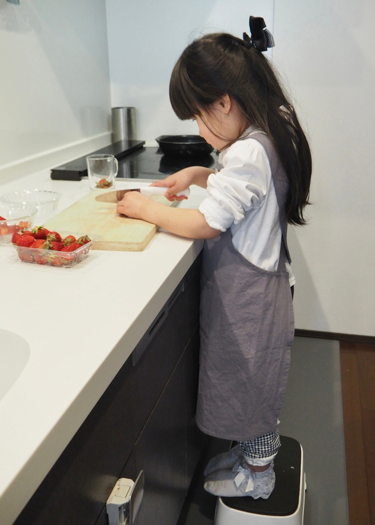 子どもがグレーのエプロンを着用してキッチンで料理をしている使用イメージ。お手伝い用エプロンとして使えるデザイン