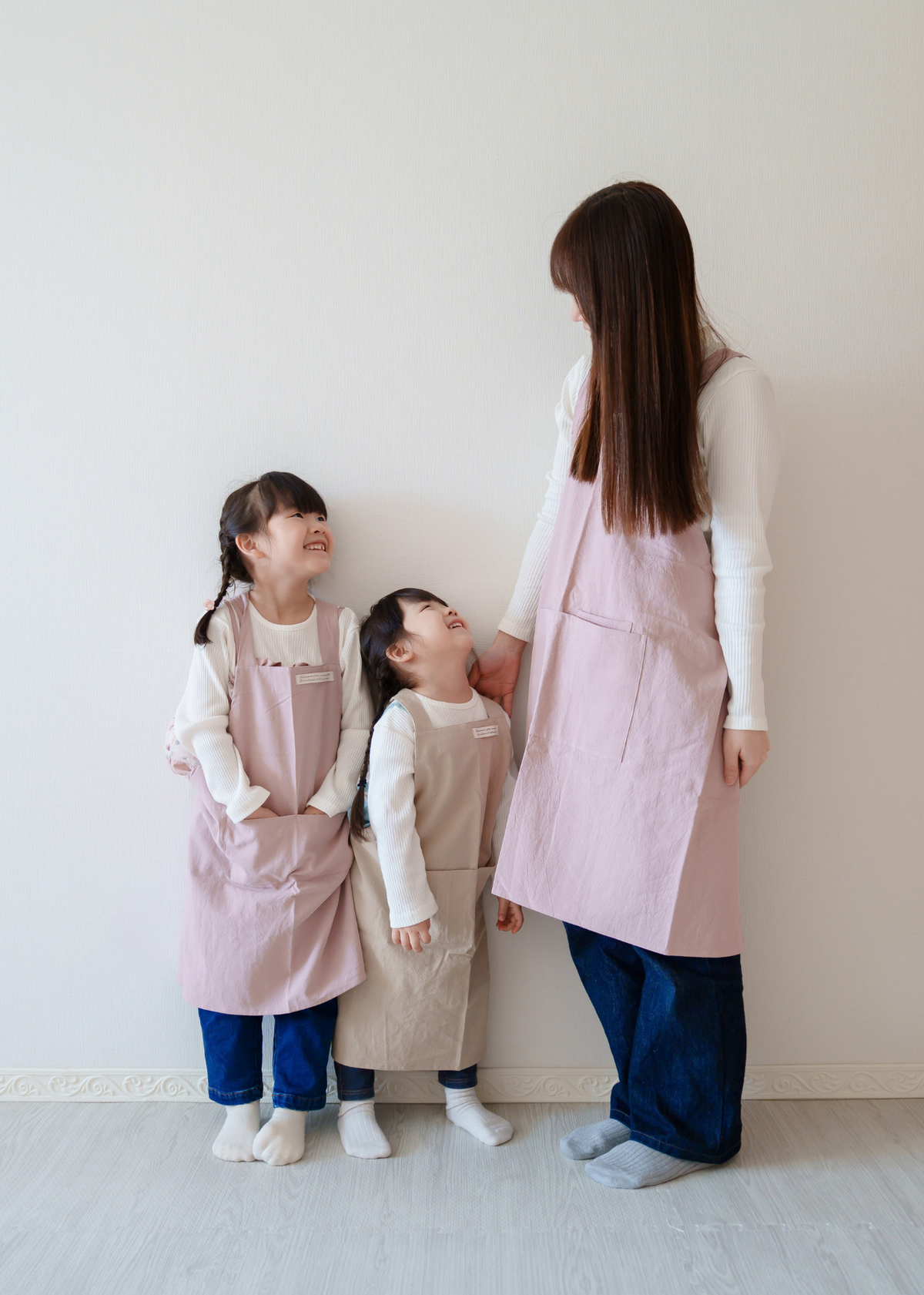母親と2人の子どもがピンク系のエプロンをお揃いで着用している使用イメージ。親子リンクコーデ