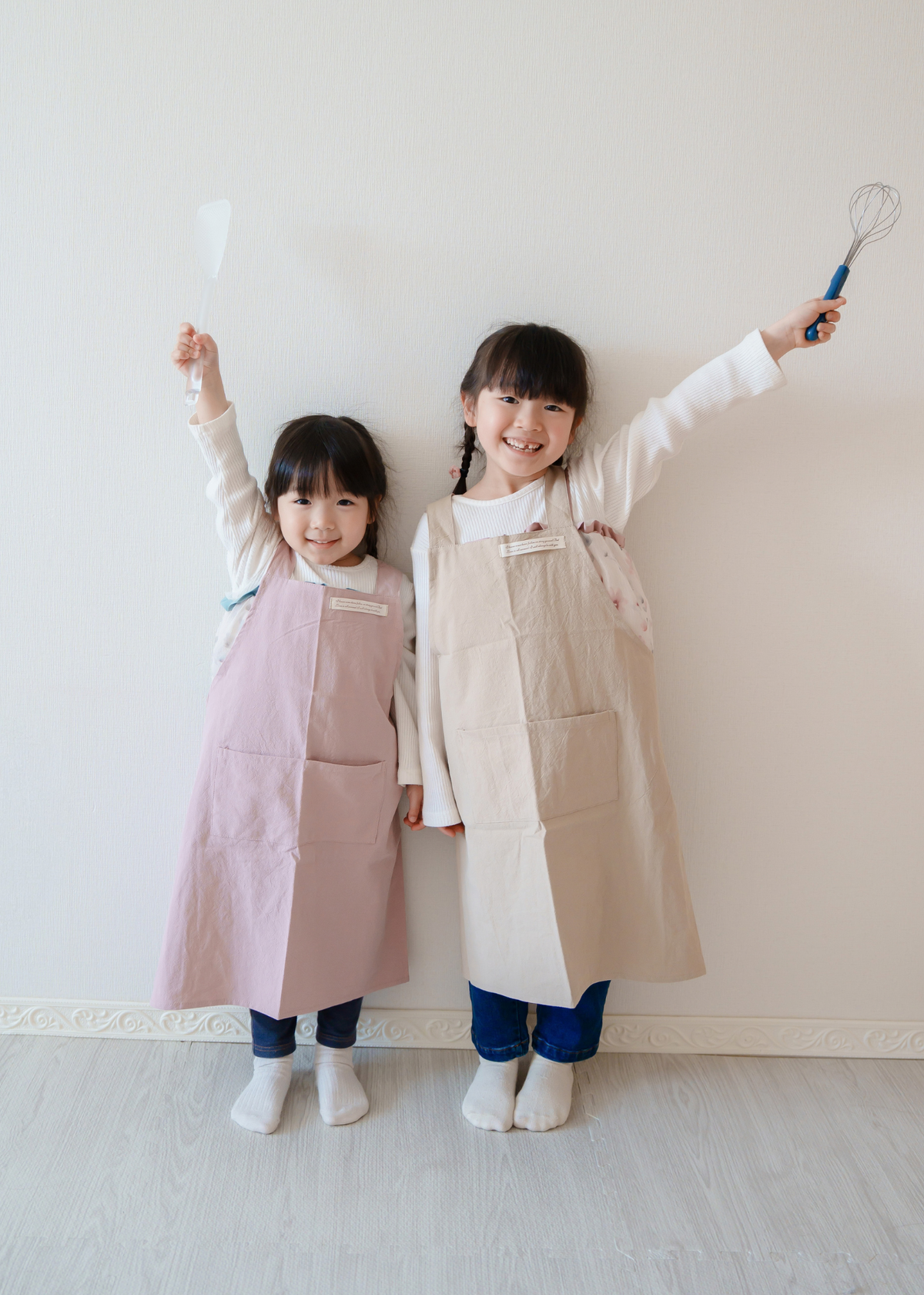 2人の子どもがピンクとベージュのエプロンを着用して並んでいる使用イメージ。きょうだいコーデ