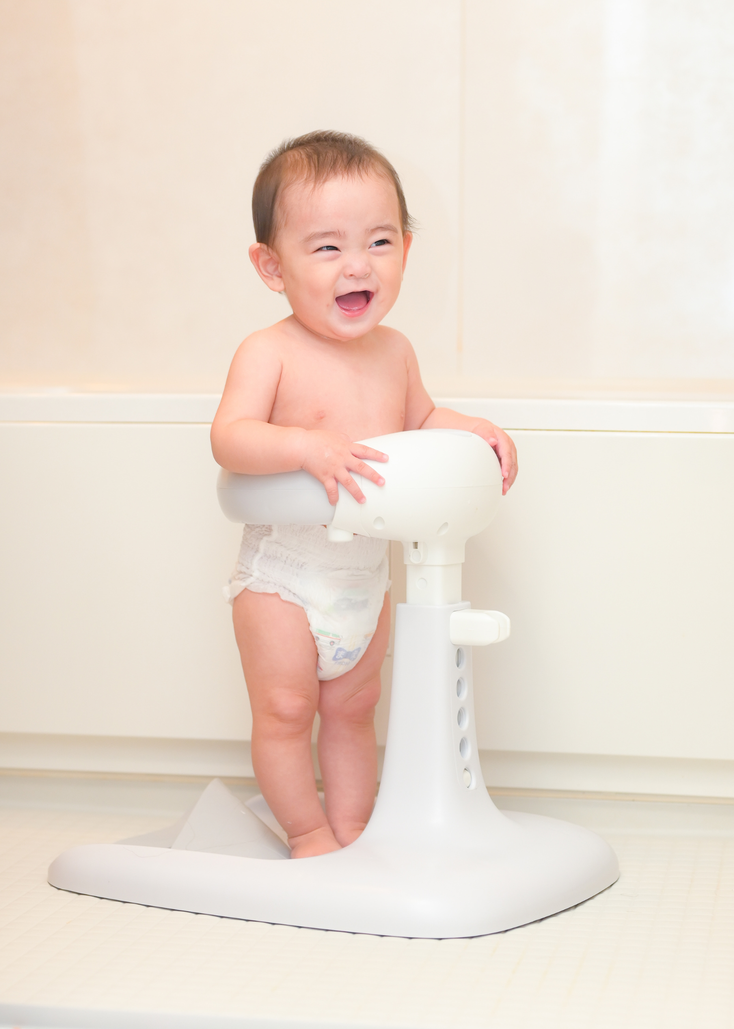 赤ちゃんがベージュのベビーシャワースタンドに座っている使用イメージ。サポートホールドで体を支える設計