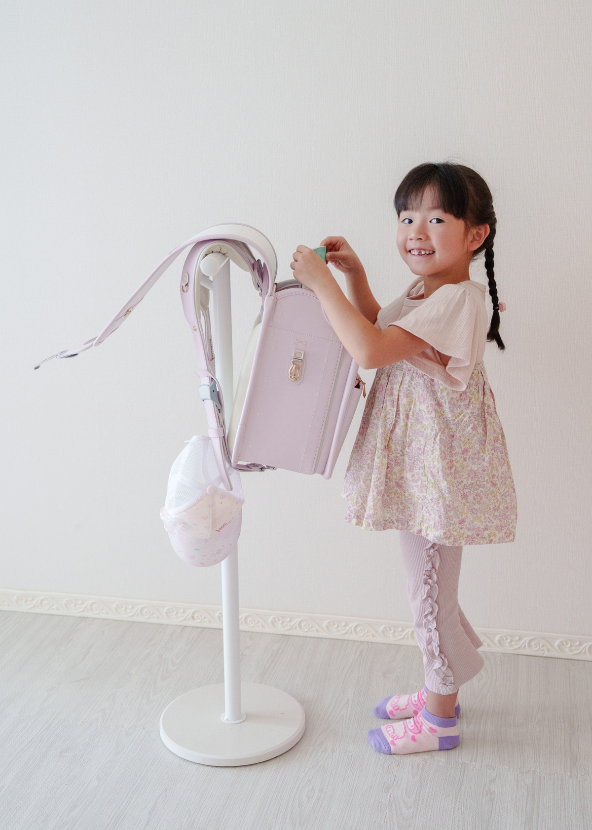 女の子がピンクのランドセルをランドセルスタンドに掛けている使用イメージ。自分で片付けやすい通学用品収納