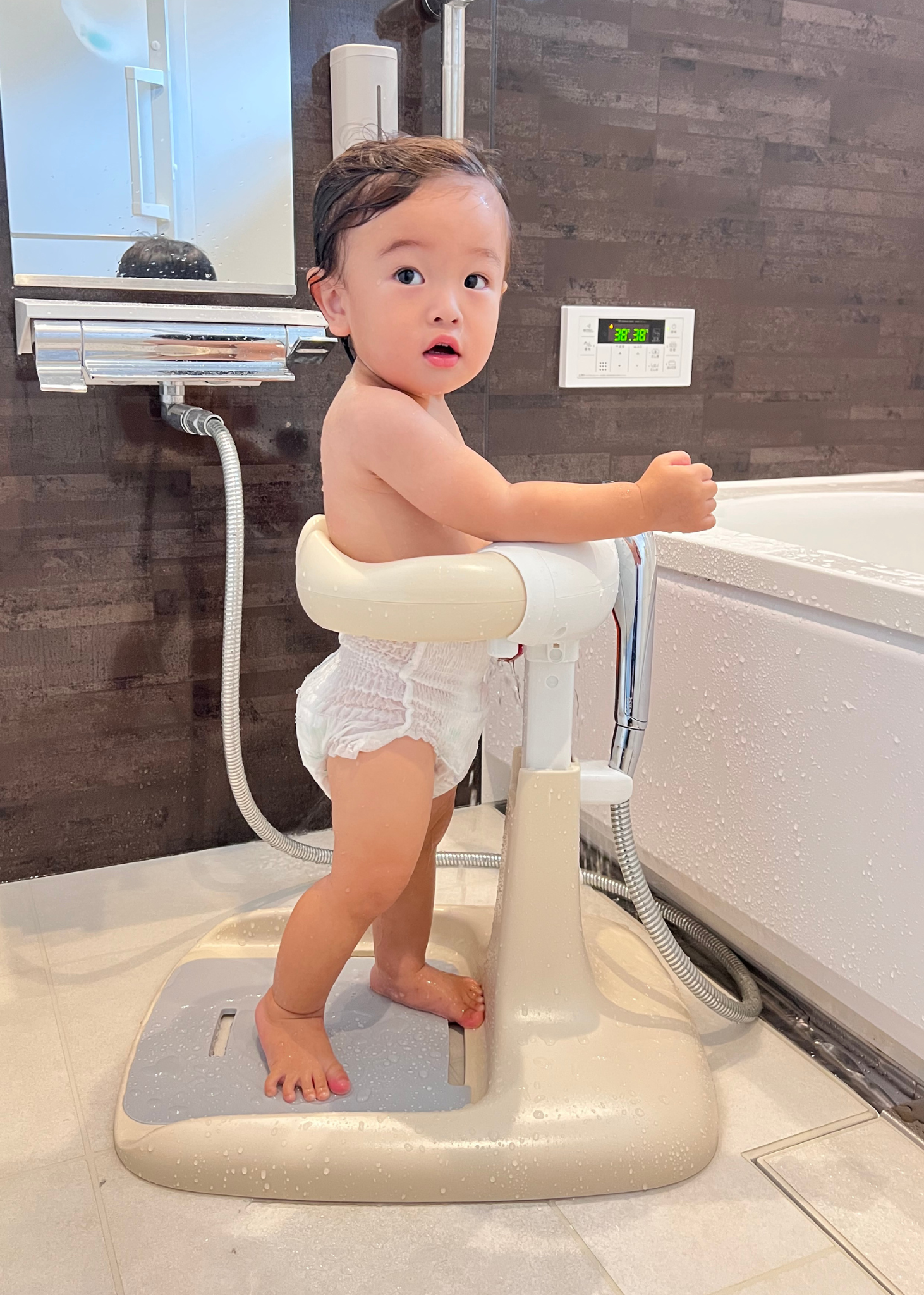 浴室で赤ちゃんがベージュのベビーシャワースタンドに座っている使用イメージ。シャワー中の姿勢を支える設計