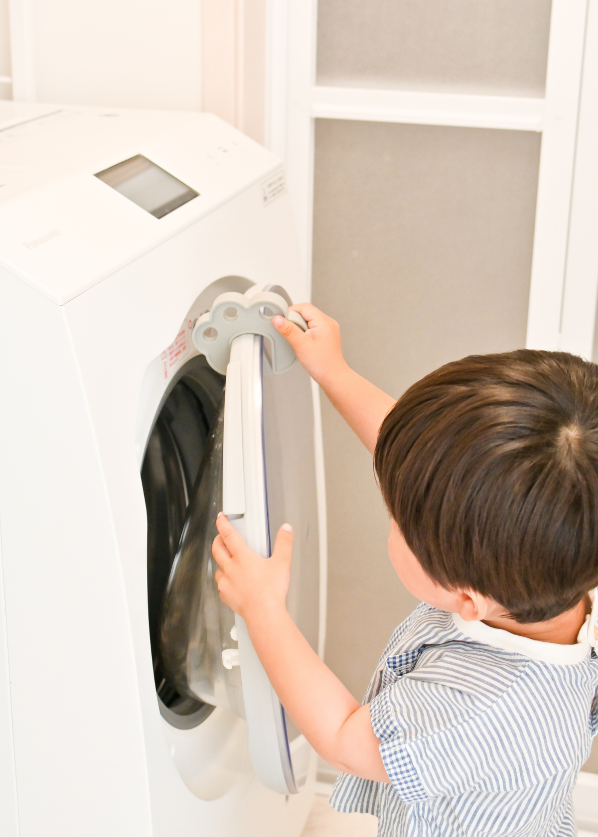 子どもが洗濯機のドア付近で肉球型指挟み防止クッションを使っている使用イメージ
