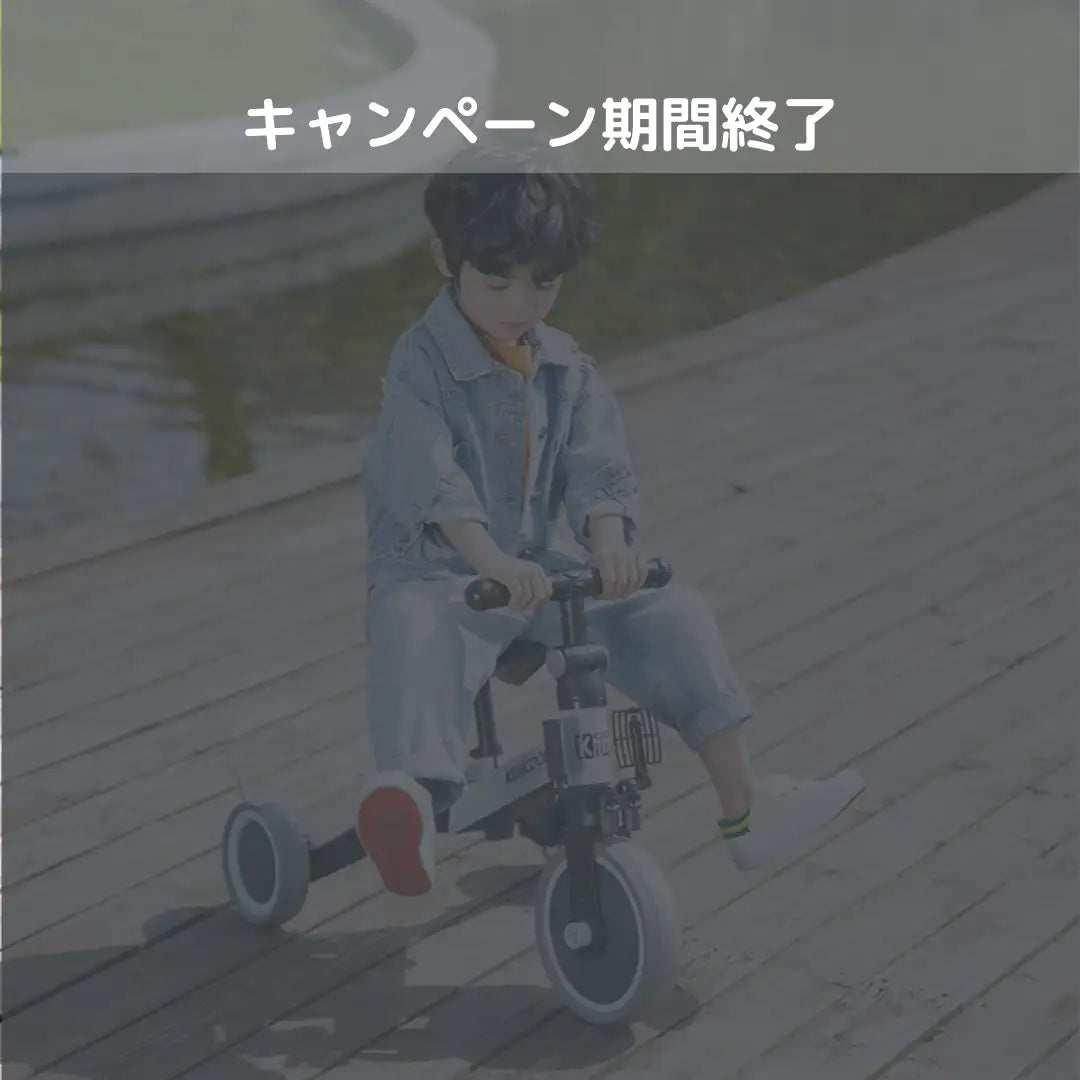 白いリムの黒と灰色の三輪バランスバイクに乗った子供。