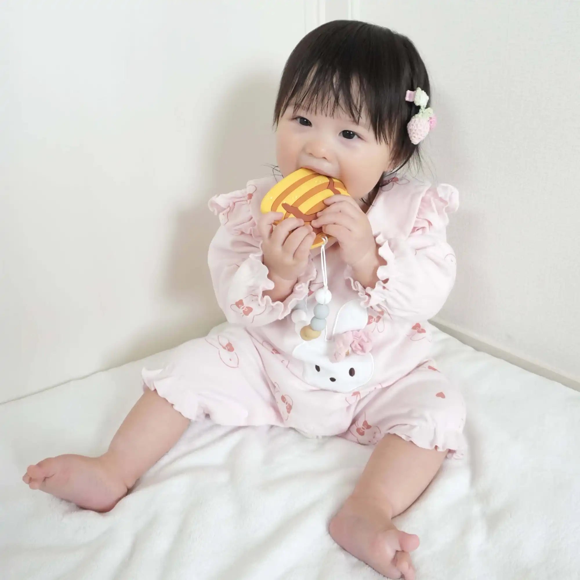 ピンクのロンパースを着た笑顔の赤ちゃんが黄色のおしゃぶりを持っている。