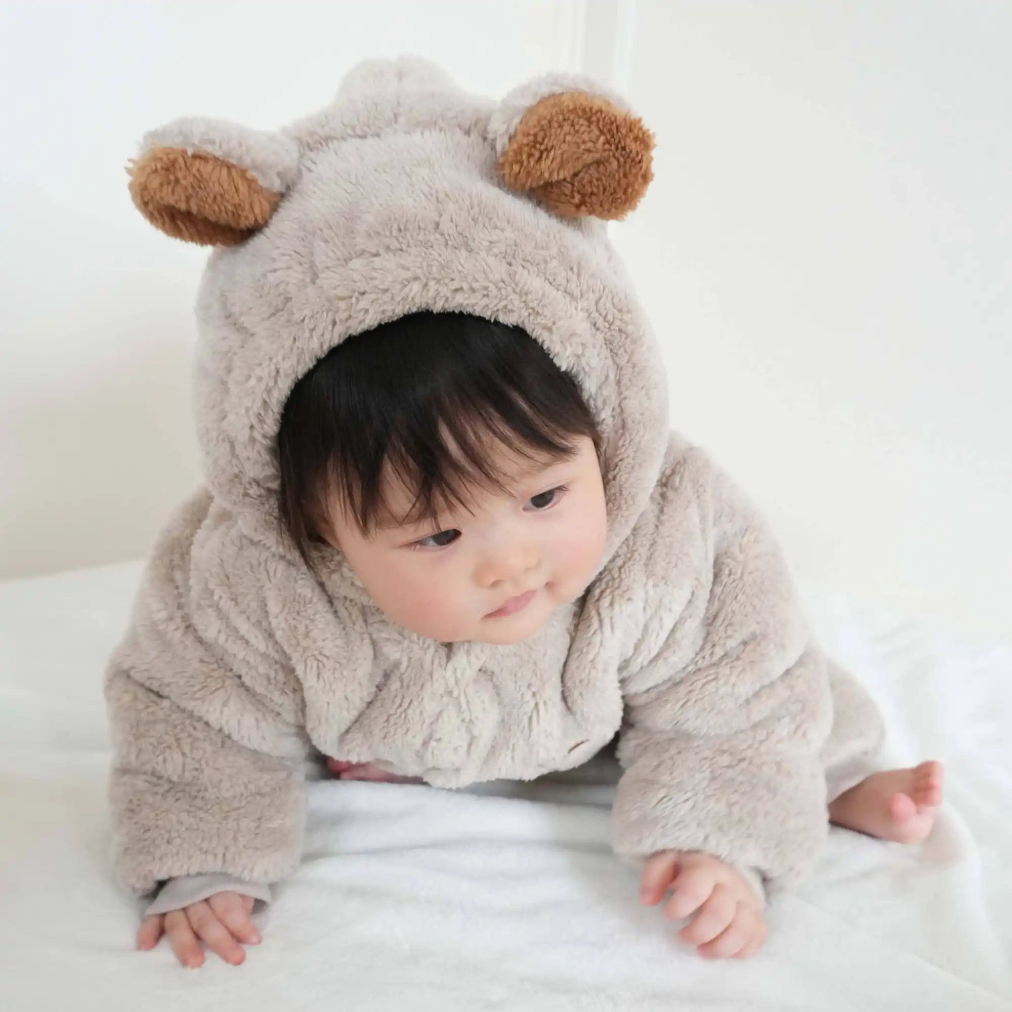 耳のついた柔らかく薄い茶色のベアコスチュームを着た赤ちゃん。