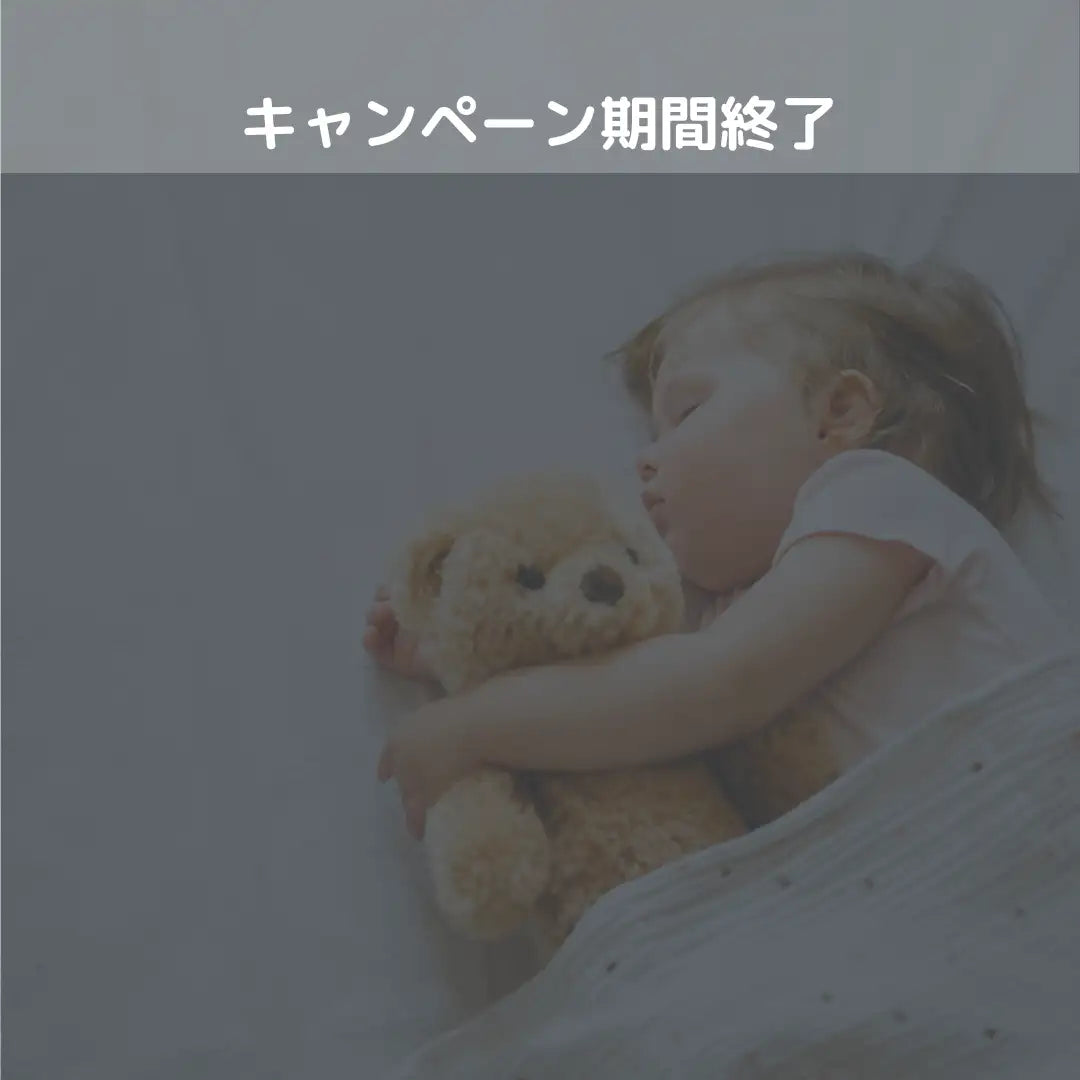 黒いボタンの目と鼻がついた柔らかいベージュのぬいぐるみのテディベアを、眠っている子供が抱きしめている。