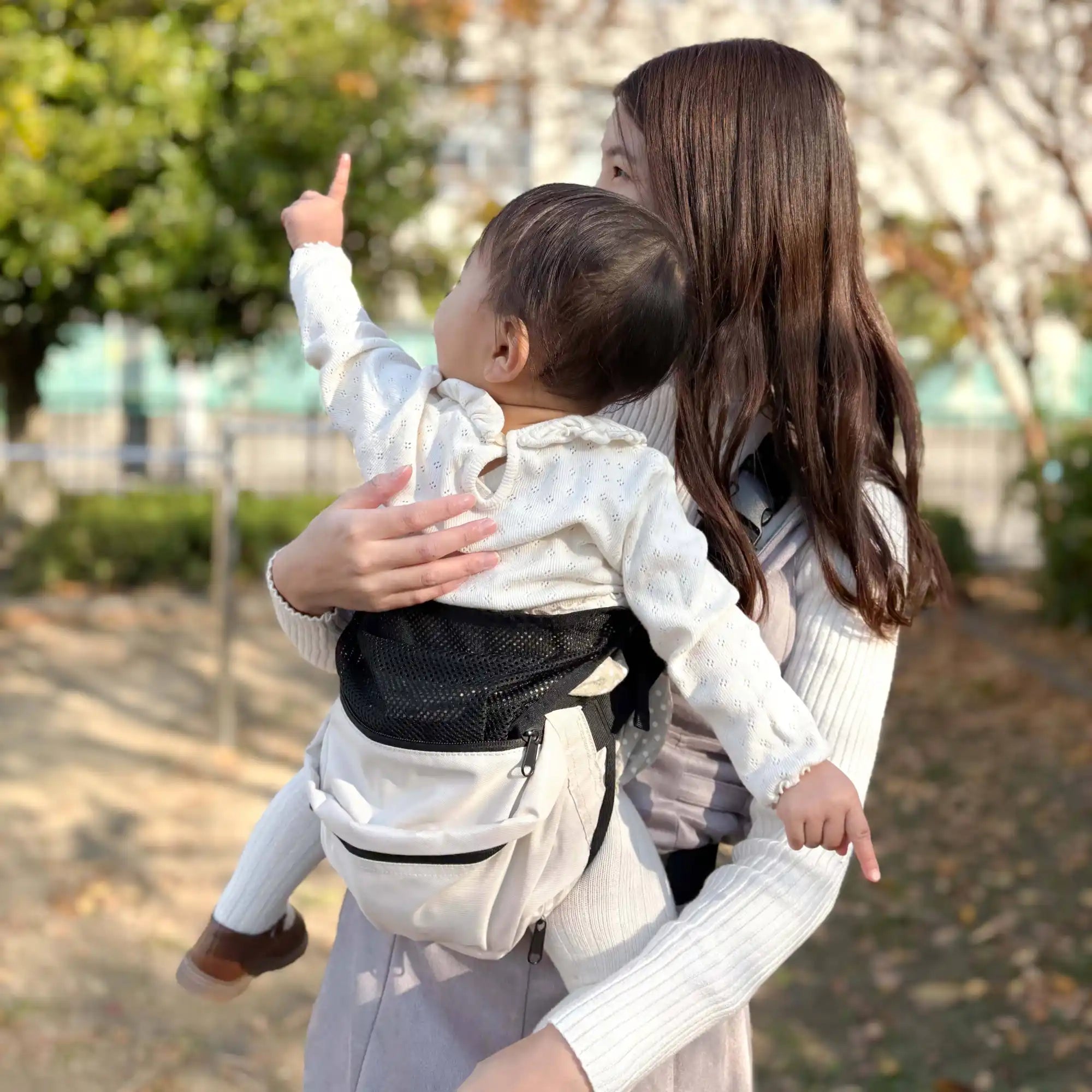 黒いメッシュの背面を持つ淡い色のベビーキャリアに赤ちゃんを抱える母親。