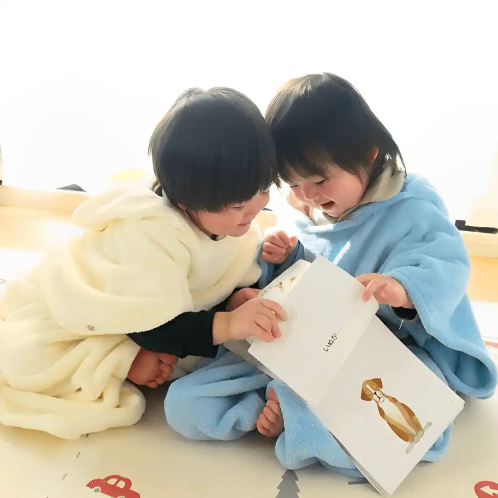 毛布にくるまった2歳児が絵本を見ている。