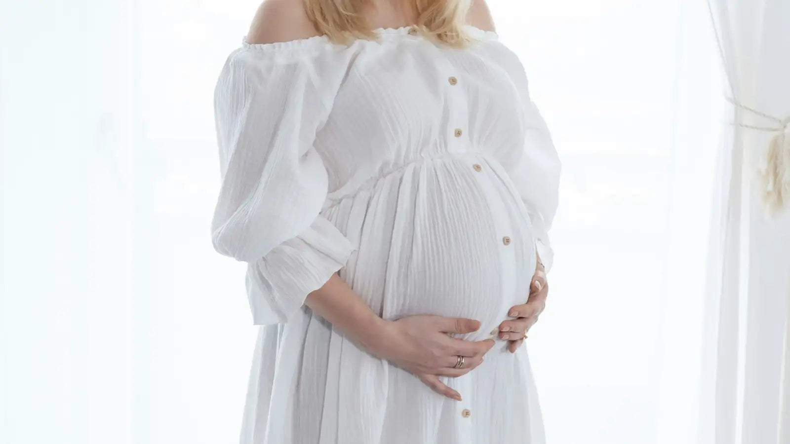 オフショルダーの白いマタニティドレスで、パフスリーブと金ボタン付き。