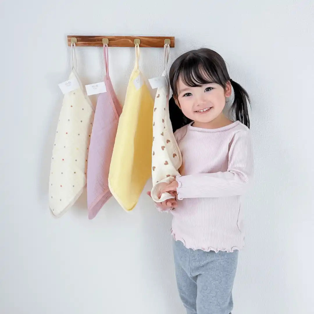 模様入りの手ぬぐいを持つ笑顔の若い女の子が、3つのカラフルな手ぬぐいが掛けられた壁掛けラックの隣に立っている。