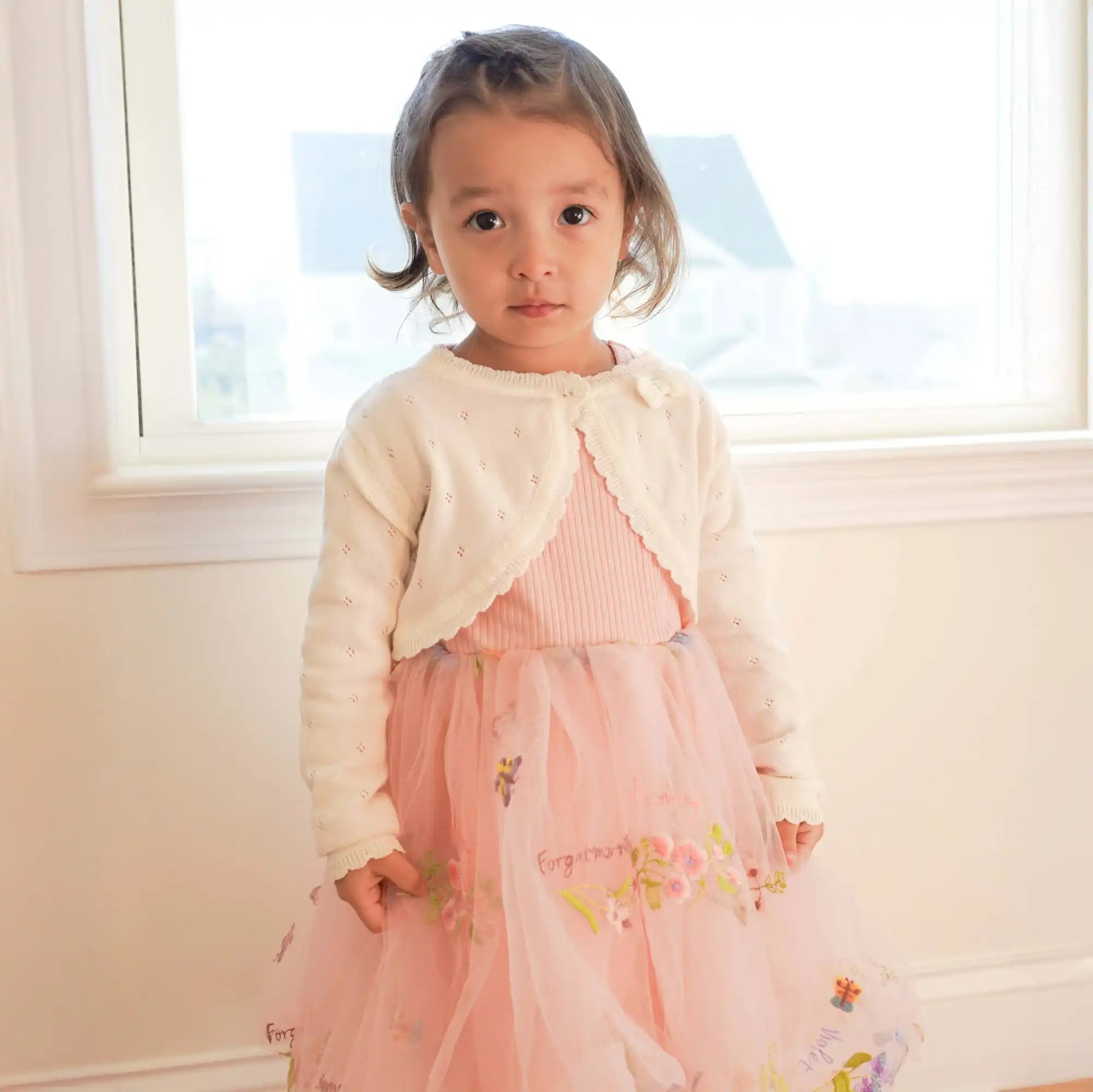 白いカーディガンを羽織ったピンクのドレスを着た若い女の子。