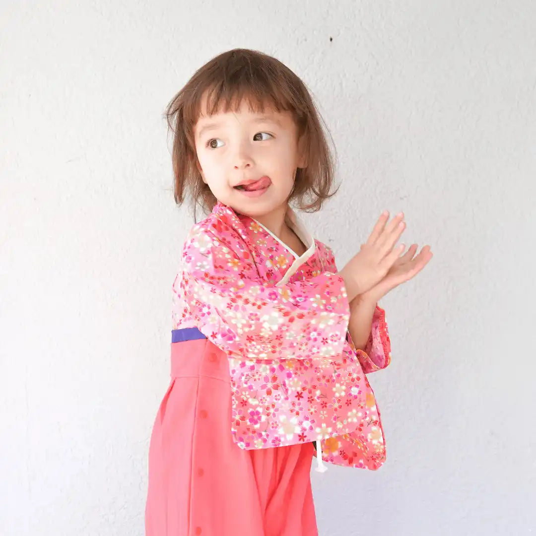 ピンクの花柄の着物とピーチ色の袴をはいた若い女の子。