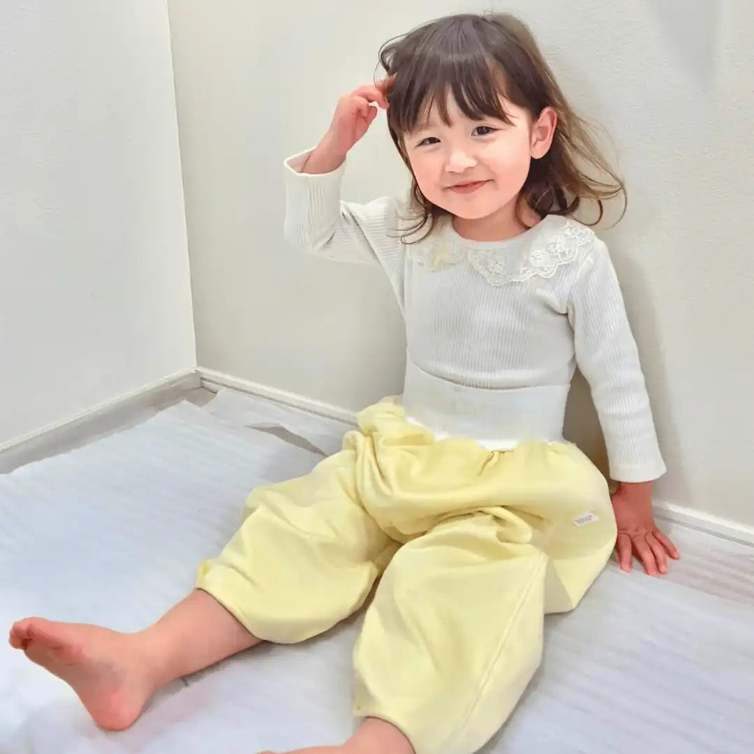 レース襟の白い長袖シャツを着て、ゆったりとした黄色いパンツを履いた幼い子供。