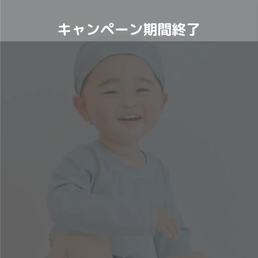 笑顔の幼児が、ライトグレーのかぶり帽とそれに合う長袖のシャツを着ている。