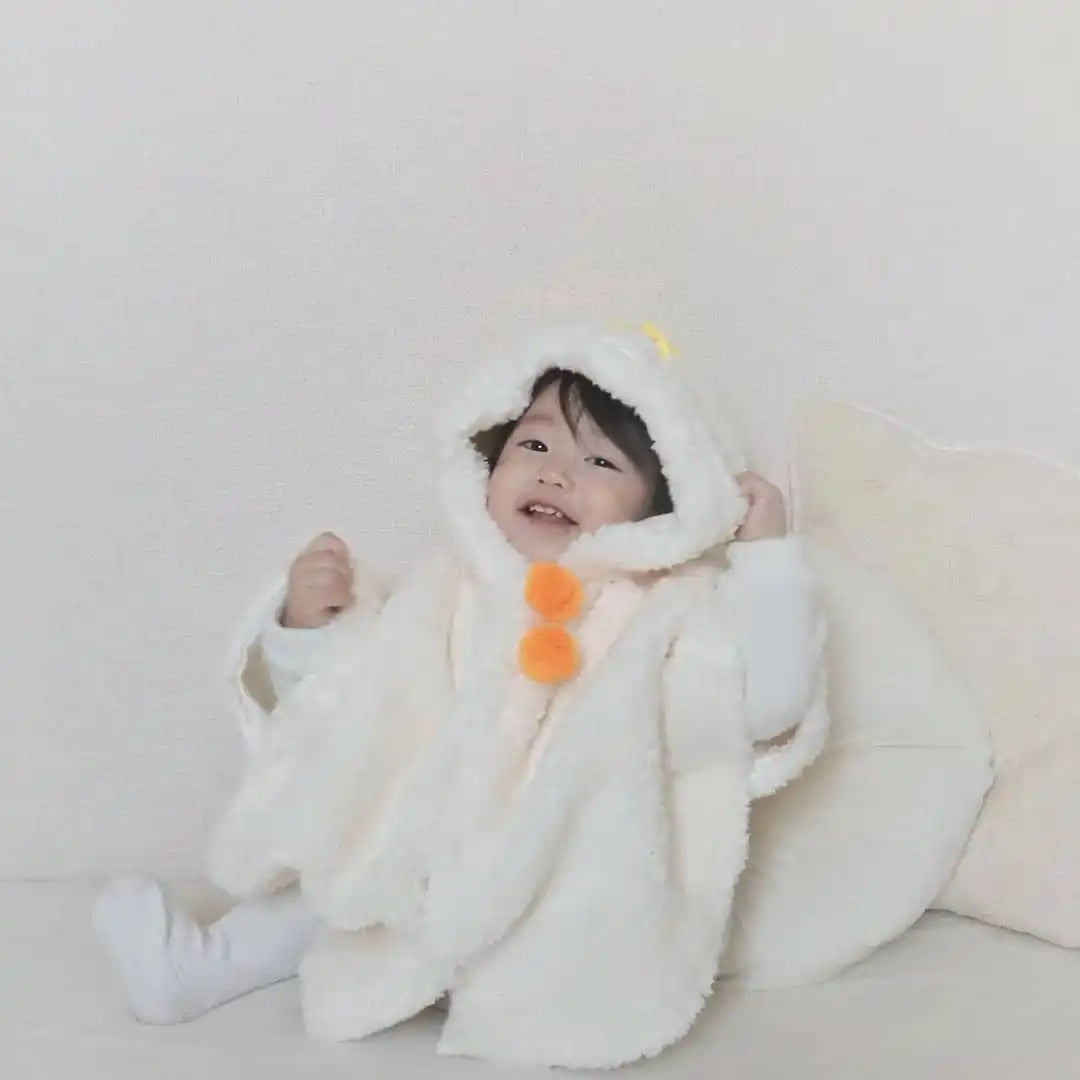 白いフード付きポンチョにオレンジのぽんぽんがついた笑顔の幼児。
