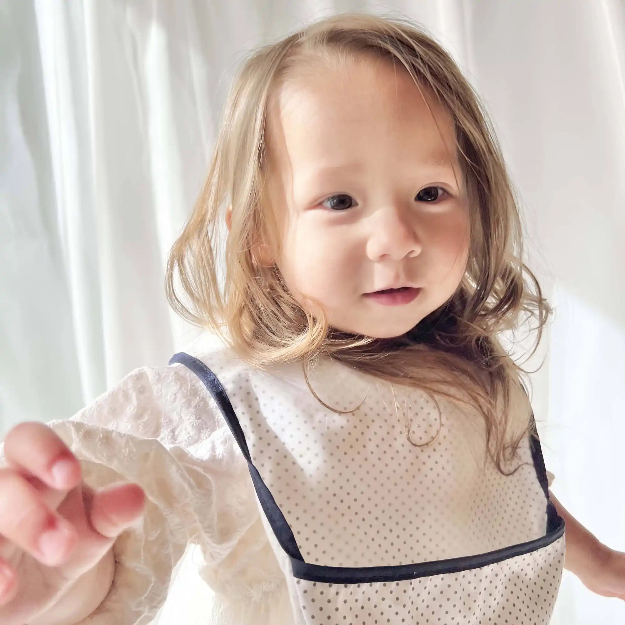 濃い縁のついた淡い色のよだれかけと長袖の白いシャツを着た幼児。