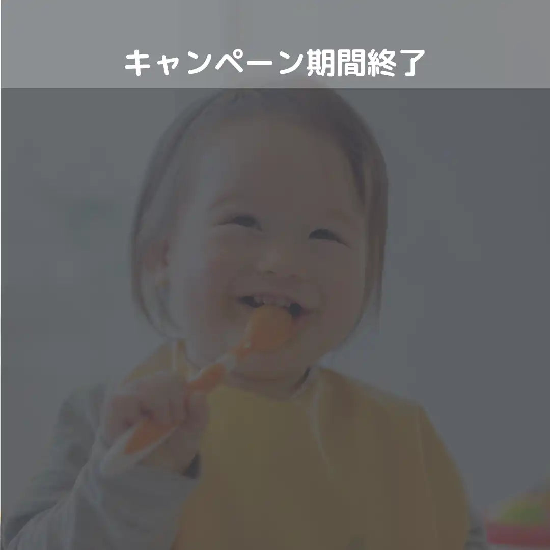 黄色のビブを着た笑顔の幼児が、オレンジ色の食べ物を口に運んでいる。