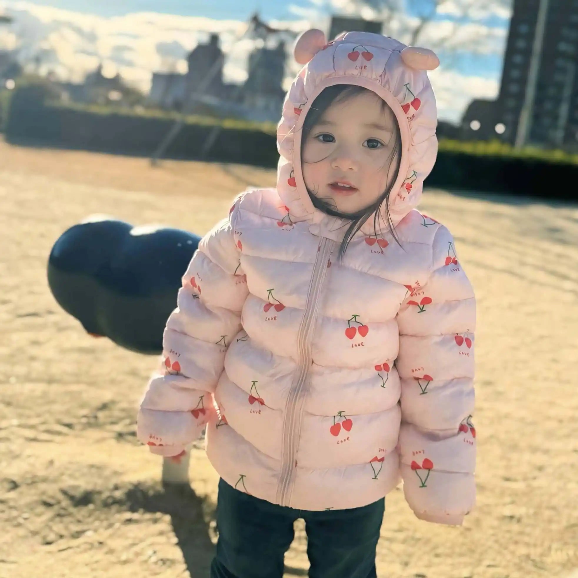 幼児用のピンクのダウンジャケットで、さくらんぼの模様とフードのクマ耳があります。